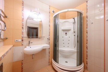 A compact bathroom with a curved glass shower cabin, wall-mounted sink, oval mirror with lighting,...