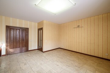 A spacious room with beige striped wallpaper, light tiled floor, wooden double door, a smaller door...