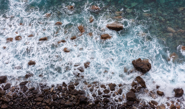 Waves crashing on rocky shoreline in Madeira, Portugal. Rugged volcanic coastline meets the Atlantic Ocean. Scenic view of the rocky cliffs and turquoise water. - Powered by Adobe