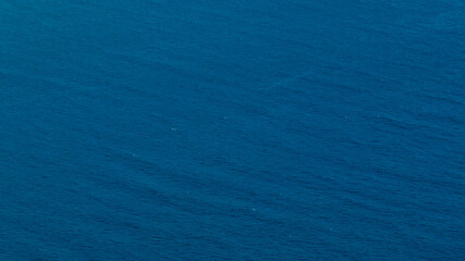 Obraz premium A deep cobalt blue sea fills the frame. The water surface is finely textured with small, rhythmic ripples, creating a mesmerizing and vast abstract maritime landscape. Ideal for textures and patterns.