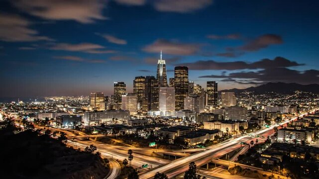 Time-lapse of the Los Angeles skyline transitioning from sunset to night with illuminated city lights and clouds