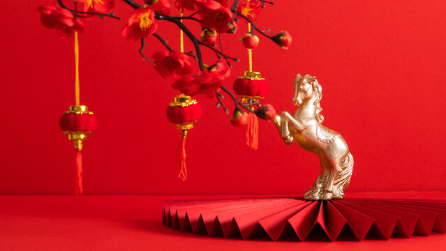 2026 Year of the Fire Horse on a red background. A plum blossom branch and traditional red lanterns, a golden horse figurine on a red paper fan, symbolizing good luck and the Spring Festival