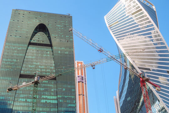 Moscow, Russia - August 15, 2025: Construction tower cranes against the backdrop of the glass towers of the Moscow City international business center.