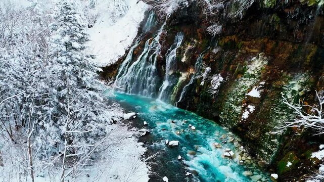 Breathtaking aerial footage of Shirahige Waterfall with turquoise water and snow-covered rocks in Biei, Hokkaido, Japan.