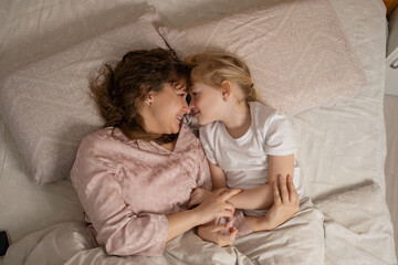 Mother and daughter lying in bed, smiling and looking into each other&rsquo;s eyes. Tender moment of love and connection.