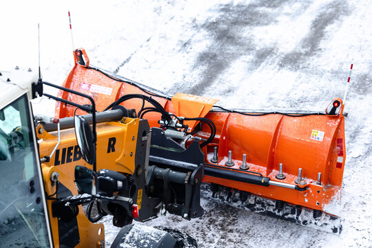 Villach, Austria - January 10, 2026: Liebherr snow plow attachment on heavy machinery clearing snow from a winter road, showcasing powerful equipment in action with vibrant orange blade