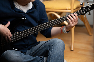 Man's hands pressing strings on a bass guitar fretboard at home, Detail shot of a person practicing...