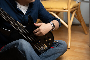 Man's hand resting on a black bass guitar while sitting cross-legged, Close up of the body and control knobs of a black electric bass guitar