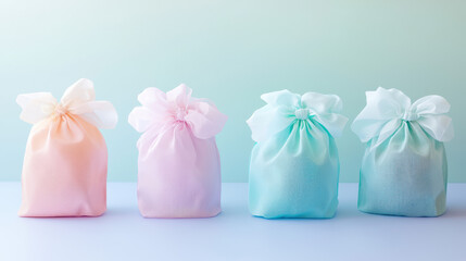 Four pastel-colored organza gift bags, orange, pink, turquoise and blue, sit in a row on a white surface against a soft teal background, creating a delicate scene.