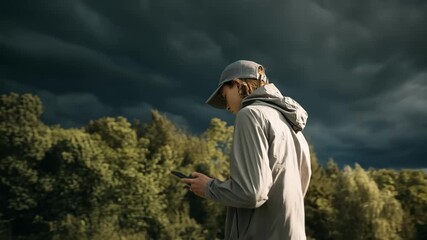 Person checking smart device outdoors while storm clouds gather illustrating preemptive weather updates for safe travel.