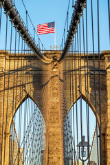 Obraz premium View of Brooklyn bridge structure in afternoon light with american flag. New York, USA.