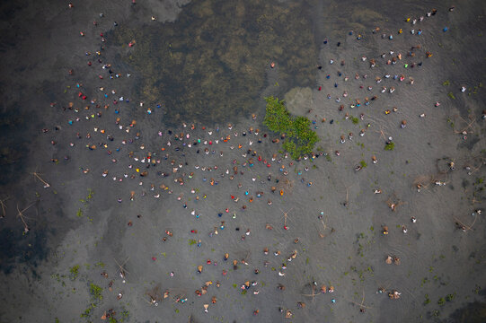 Pabna, Bangladesh - 05 December 2020: Aerial view of people scattered across a vast expanse of mud, their colorful clothing creating a vibrant mosaic against the muted earth tones.