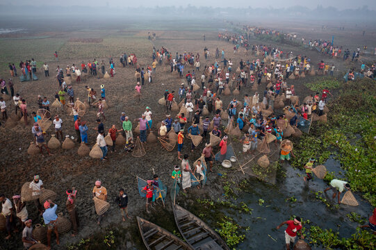 Pabna, Bangladesh - 05 December 2020: Aerial view of a multitude of figures scattered across the landscape, each carrying sacks amidst the murky earth and waterways.