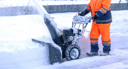 A janitor removes snow after a snowfall on the street with a snow blower
