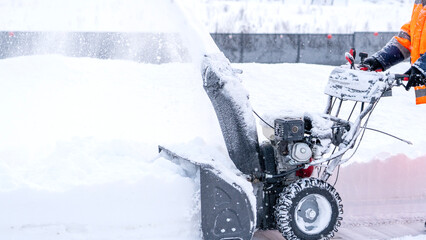 A janitor removes snow after a snowfall on the street with a snow blower