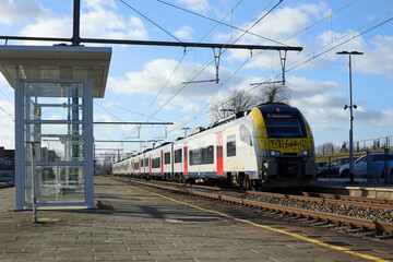 Modern passenger train arriving at a station platform on a sunny day with blue skies, ready for departure or arrival.