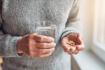 Senior man holding glass of water and supplements for andropause hormonal balance, promoting healthy lifestyle and wellness in natural light