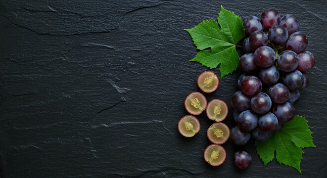 Dark blue grapes with cross sections and green foliage on black slate board for wine tasting and fruit shop promotional material