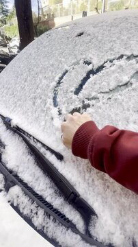 Dibujando con nieve un coraz&oacute;n en parabrisas de coche y cogiendo hielo en d&iacute;a nevado y fr&iacute;o