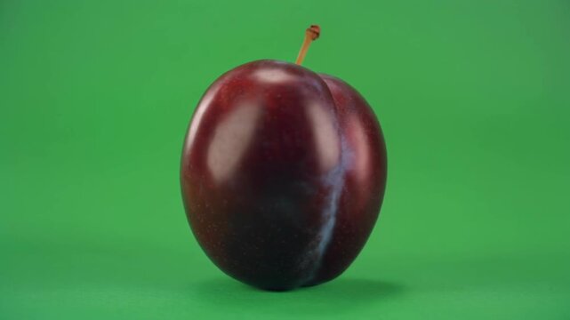 A shiny, dark red apple with a small stem against a solid green background with a slight shadow.