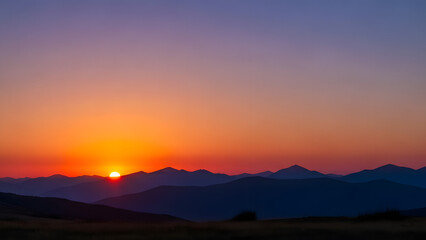 Obraz premium Distant sun rising over silhouetted mountain range creating vibrant orange and purple gradient sky
