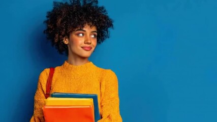 A radiant young person with vibrant curly hair smiles confidently, holding a stack of colorful textbooks against a striking blue background. This engaging studio portrait evokes enthusiasm for learnin