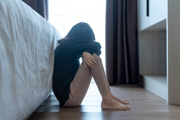 A depressed young girl sitting on a bedroom floor with her head on her knees. Mental health, sadness, solitude, and emotional distress concept.