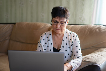 Serious mature woman wearing glasses working on laptop online