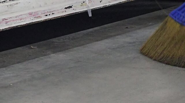 Sweeping the Floor: A close-up shot of a broom sweeping a concrete floor, capturing the act of cleaning and maintaining cleanliness.