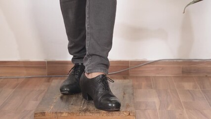 Cropped view of a person wearing black leather shoes and gray pants on an indoor floor, making a flamenco dance steps demonstration