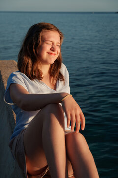 Happy young woman squinting in the bright sun by the sea in Petrovac, Montenegro. Close up portrait, joyful emotion, summer vacation and mediterranean heat.