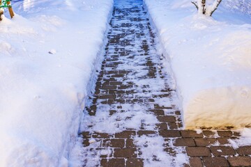 Beautiful view of cleared brick walkway between deep snow banks in residential garden during winter. Sweden.