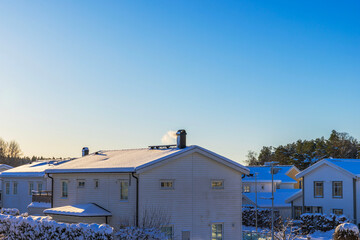 Beautiful view of snow covered villas with smoking chimneys against blue sky. Sweden.