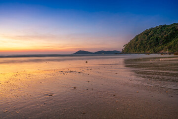 Beautiful tropical beach at sunset with golden light reflecting on the wet sand under a vibrant twilight sky