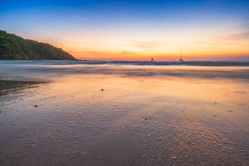 Beautiful tropical beach at sunset with golden light reflecting on the wet sand under a vibrant twilight sky