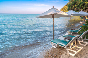 Beach chairs and umbrellas lined up on a serene tropical beach with crystal clear blue water