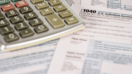 A person works on 1040 tax forms using a calculator in a home office.