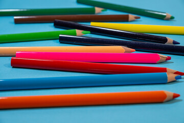 Fototapeta premium a scattered assortment of sharpened colored pencils in shades of orange, blue, red, and green resting on a solid blue background.