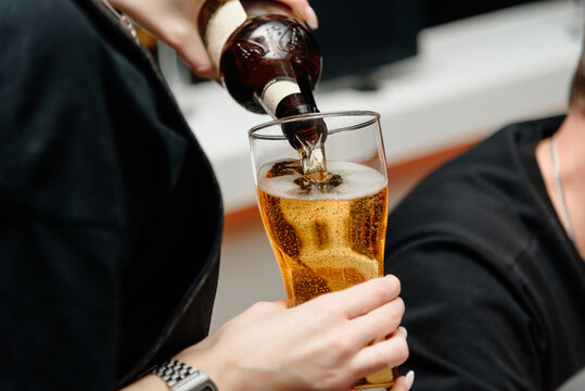 waitress pours light beer into large beer mug for customer at bar, close-up view of bartender hand holding mug and bottle - Powered by Adobe