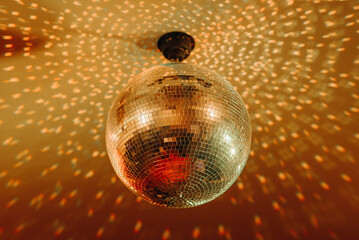 Obraz premium disco ball with mirror surface and bright rays, orange color, hanging on ceiling, night party background