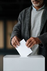 Caucasian mature male voting by placing ballot in box during election