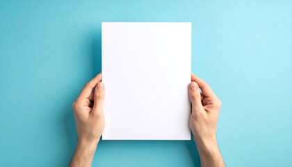 Obraz premium Hands holding blank white paper on blue background for mockup.