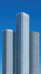 Fototapeta premium Three modern skyscrapers of varying shapes ascend against a clear, vibrant blue sky