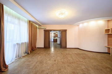 Fototapeta premium A spacious room with beige tiled flooring, large windows with sheer white and golden curtains, a crystal chandelier, wooden door frames, and built-in shelves. Light and airy