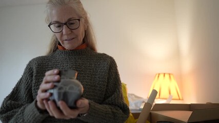 Mature woman opens a box filled with family heirlooms and travel items, recalling memories and stories tied to each piece.