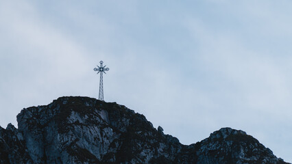 Metal cross on top of mountain against blue sky, symbol of faith, spiritual pilgrimage site, concept of hope, religion, freedom and meditation in nature.