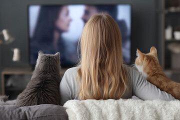 Woman and her two cats watching romantic movie on tv on a couch at home, view from back