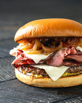 Beef Burger with Melted Cheese, Caramelized Onions and Pastrami on Dark Wooden Background
