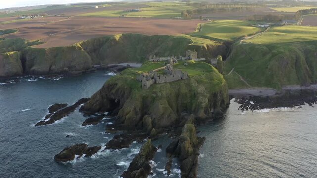 Aerial view of Dunnottar Castle ruins perched on cliffs overlooking the sea, displaying the contrast between the castle and the surrounding landscape, Stonehaven, Scotland, United Kingdom.