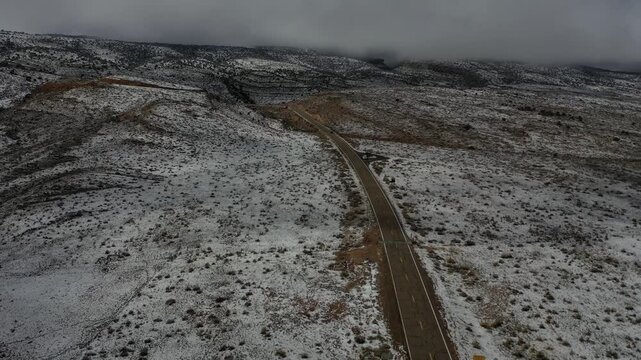 Aerial view of a road bisecting a winter landscape, where snow dusts the hills under a moody sky, creating a stark contrast, Albuquerque, New Mexico, United States.